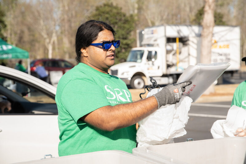 A man holds an empty trash bag and a folder labeled "TRASH" over a bin.